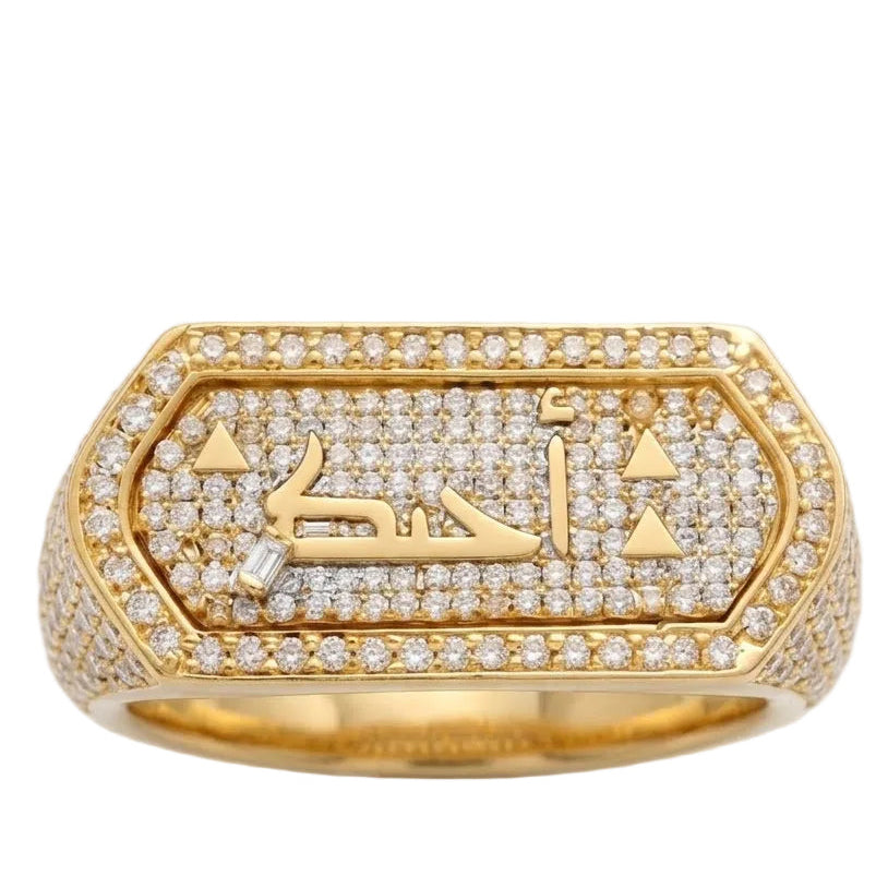 A gold signet ring paved with small clear stones, featuring Arabic calligraphy in the center, shown on a light gray background.